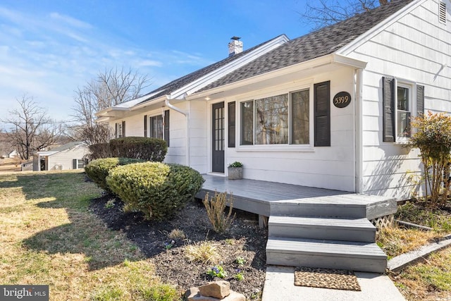 entrance to property with a lawn, roof with shingles, and a chimney