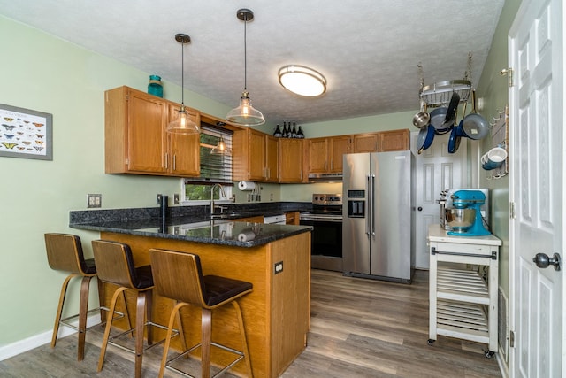 kitchen with a breakfast bar, hanging light fixtures, appliances with stainless steel finishes, kitchen peninsula, and hardwood / wood-style flooring