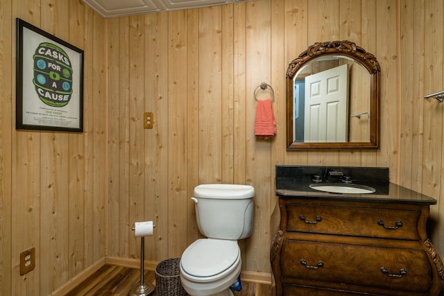 bathroom with hardwood / wood-style flooring, vanity, wood walls, and toilet