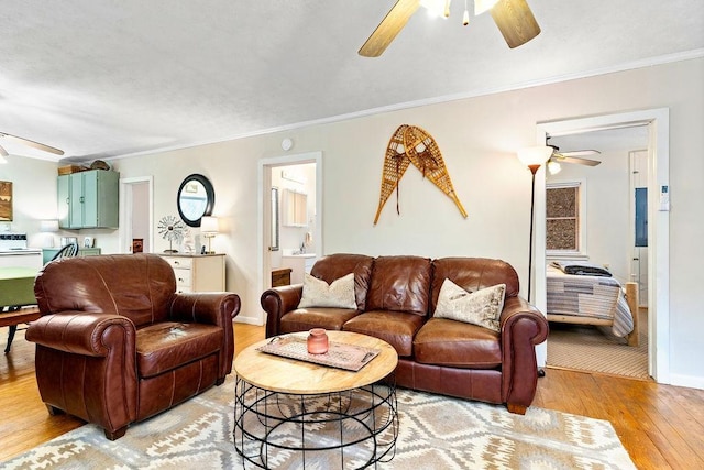 living area featuring baseboards, a ceiling fan, light wood-type flooring, and ornamental molding