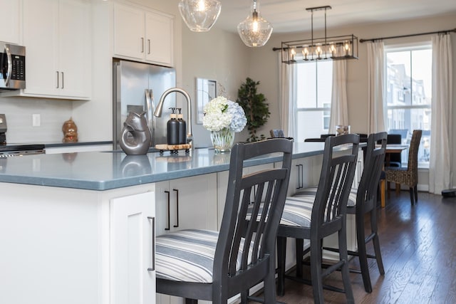 kitchen featuring dark wood-style floors, stainless steel appliances, hanging light fixtures, white cabinets, and dark countertops