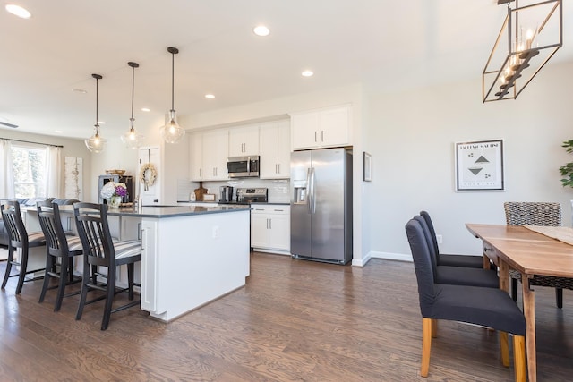 kitchen featuring dark wood-type flooring, appliances with stainless steel finishes, a kitchen bar, dark countertops, and backsplash