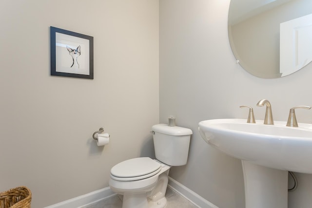 half bathroom featuring tile patterned floors, toilet, baseboards, and a sink