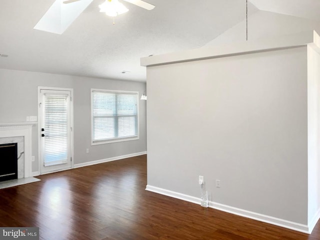 unfurnished living room with dark wood-type flooring, a fireplace, lofted ceiling with skylight, and ceiling fan