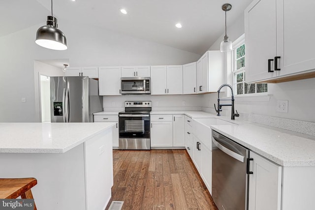 kitchen featuring pendant lighting, appliances with stainless steel finishes, white cabinetry, a sink, and light stone countertops