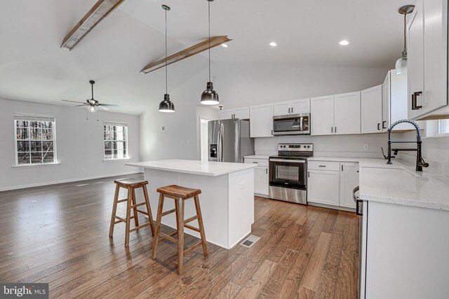 kitchen featuring dark wood-type flooring, sink, appliances with stainless steel finishes, a kitchen island, and white cabinets