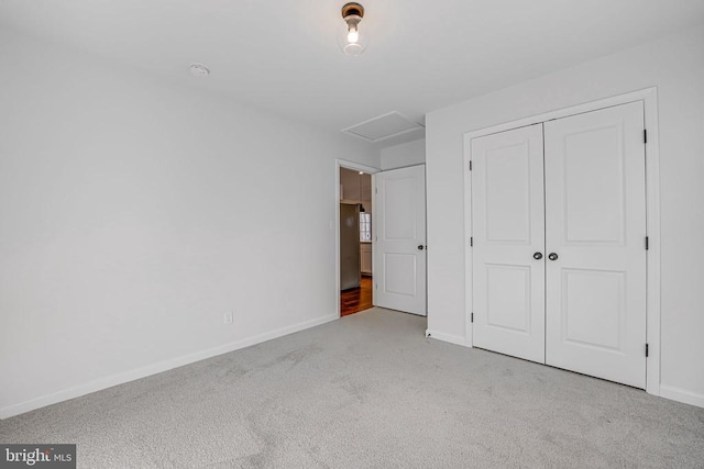 unfurnished bedroom featuring attic access, a closet, light colored carpet, and baseboards