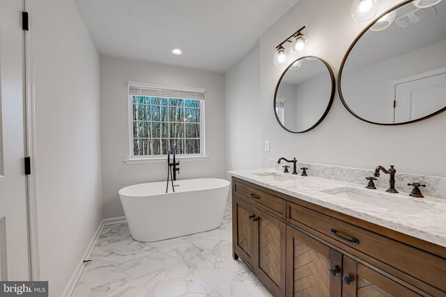 full bathroom featuring double vanity, baseboards, marble finish floor, a freestanding bath, and a sink