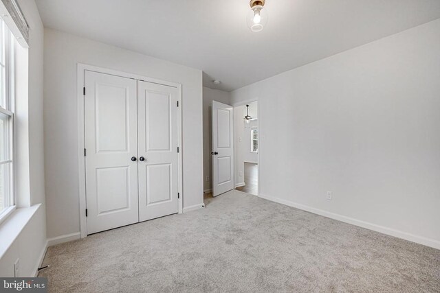 unfurnished bedroom featuring light colored carpet, a closet, multiple windows, and baseboards