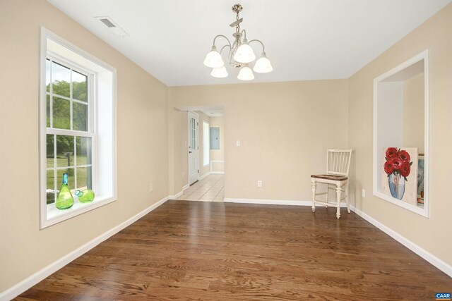 unfurnished dining area with wood-type flooring, electric panel, and a notable chandelier