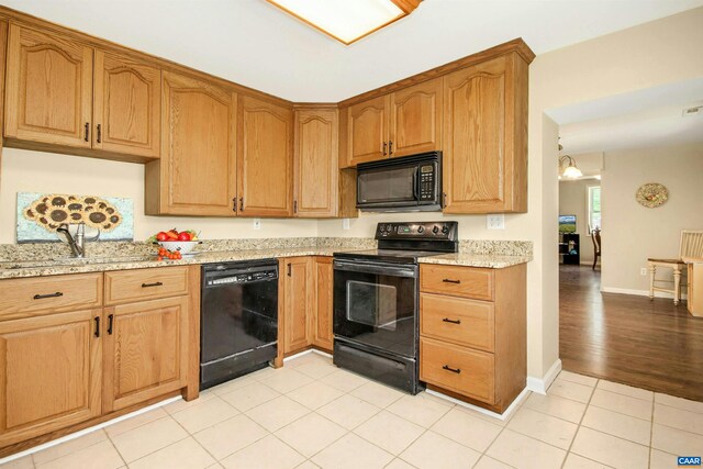 kitchen featuring light stone countertops, light tile patterned floors, black appliances, and sink