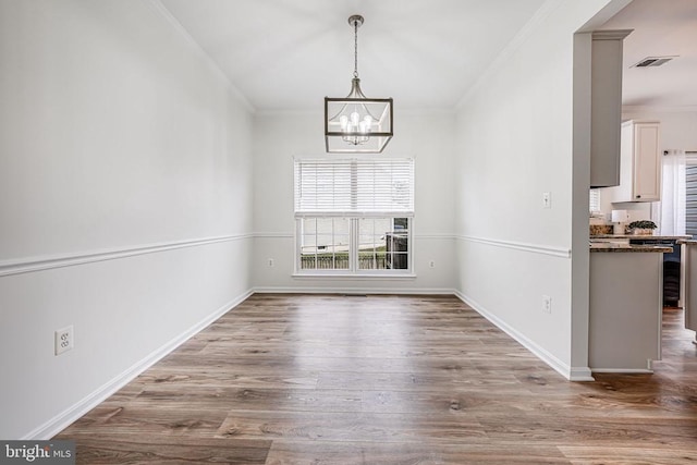 unfurnished dining area with crown molding, visible vents, an inviting chandelier, wood finished floors, and baseboards