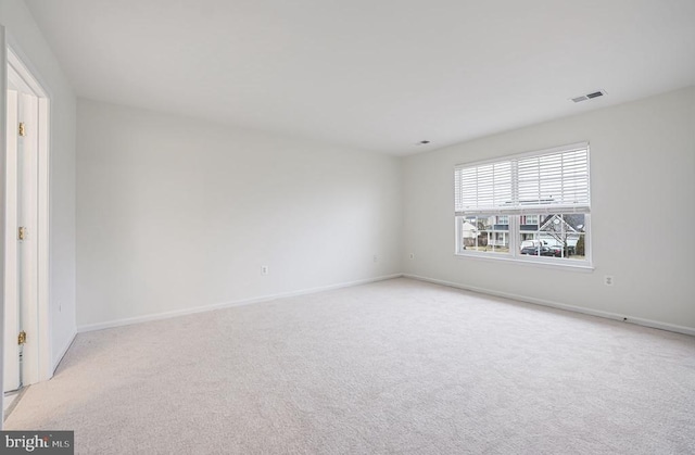 spare room featuring light carpet, visible vents, and baseboards