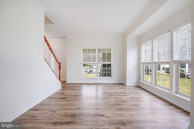 spare room with stairs, wood finished floors, a wealth of natural light, and baseboards