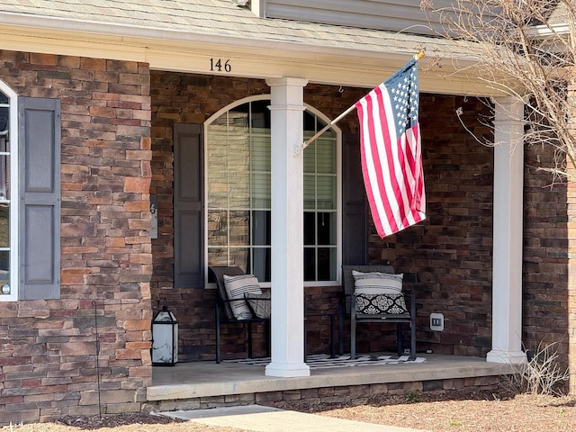 entrance to property with covered porch, brick siding, and roof with shingles