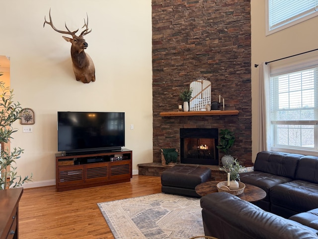 living room featuring baseboards, a fireplace, a high ceiling, and wood finished floors