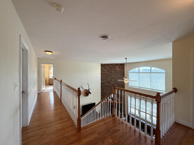 hall with wood finished floors, an upstairs landing, visible vents, and baseboards