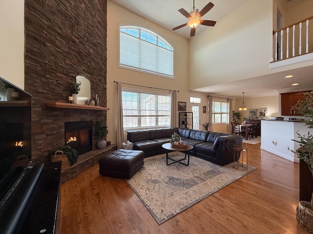 living area with ceiling fan, a stone fireplace, baseboards, and wood finished floors