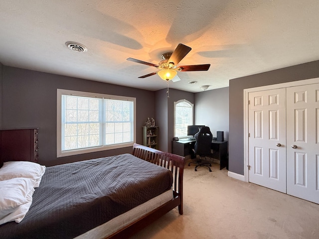 bedroom with light carpet, visible vents, ceiling fan, a textured ceiling, and a closet