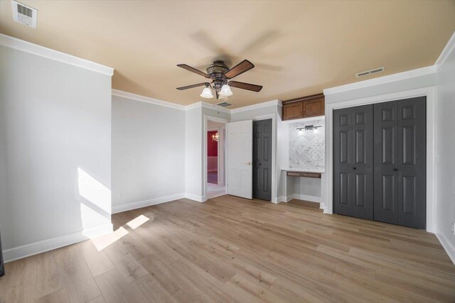 unfurnished bedroom featuring crown molding, two closets, visible vents, light wood-type flooring, and baseboards