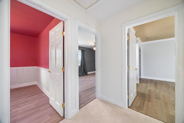 corridor with light carpet, light wood-style flooring, baseboards, and crown molding