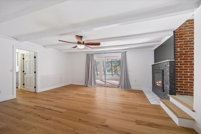 unfurnished living room featuring wood finished floors, a ceiling fan, a fireplace with flush hearth, baseboards, and beam ceiling