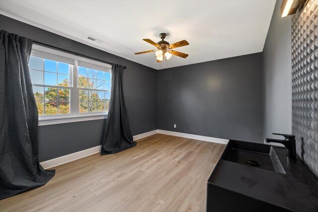 unfurnished room with baseboards, light wood-style flooring, visible vents, and a sink