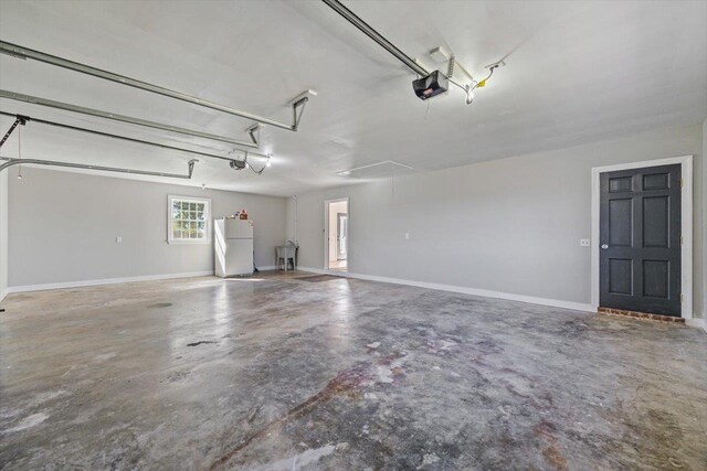 garage with a garage door opener, freestanding refrigerator, a sink, and baseboards