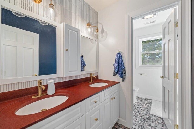 bathroom with visible vents, a sink, toilet, and double vanity