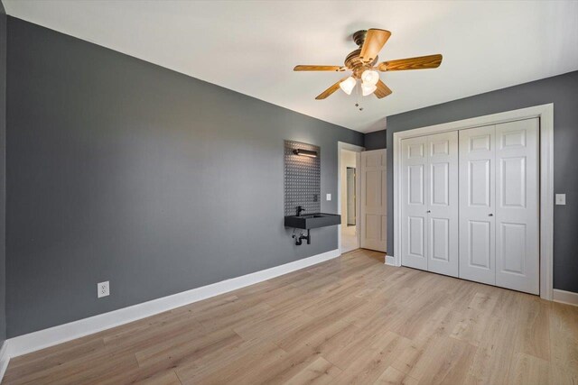 unfurnished bedroom featuring a closet, ceiling fan, light wood finished floors, and baseboards