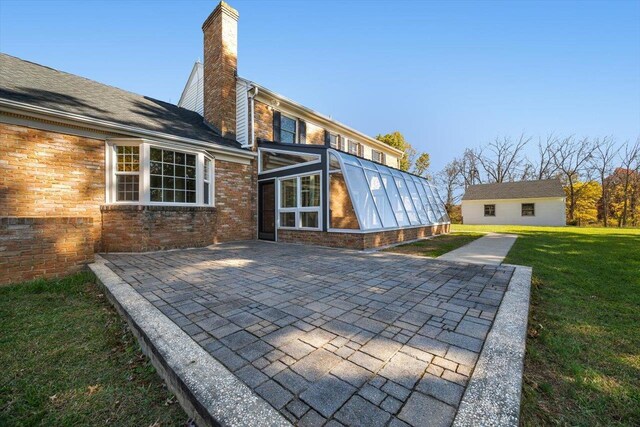 back of property featuring a patio, brick siding, a sunroom, a lawn, and a chimney