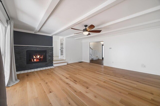 unfurnished living room with light wood-type flooring, a lit fireplace, stairway, and beamed ceiling