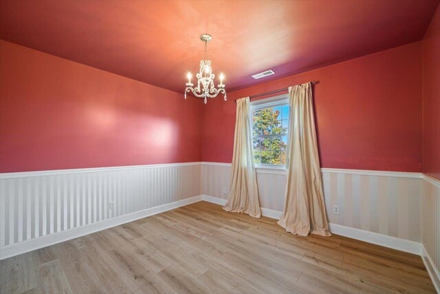 empty room featuring a chandelier, a wainscoted wall, visible vents, and wood finished floors