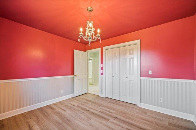 unfurnished bedroom featuring a notable chandelier, a closet, wood finished floors, and wainscoting