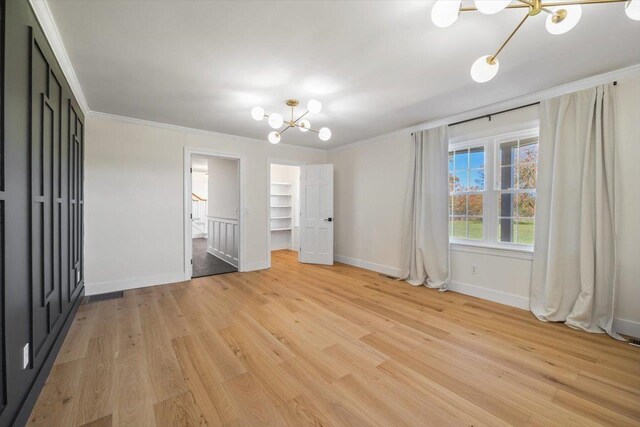 unfurnished bedroom with a walk in closet, a notable chandelier, light wood-style flooring, ornamental molding, and baseboards