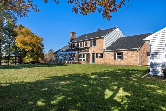 rear view of house featuring a sunroom, a chimney, brick siding, and a yard