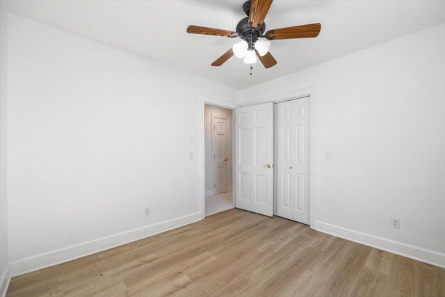 unfurnished bedroom featuring a ceiling fan, a closet, light wood-style flooring, and baseboards