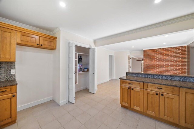 kitchen featuring brown cabinets, ornamental molding, backsplash, and dark stone countertops