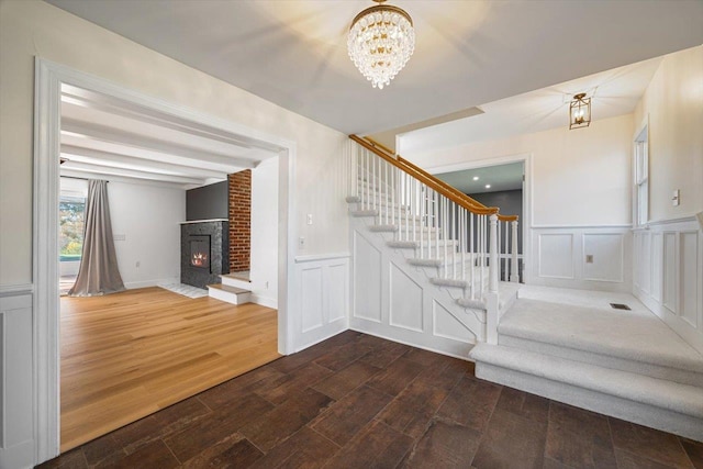 stairway featuring visible vents, wood finished floors, an inviting chandelier, a brick fireplace, and a decorative wall