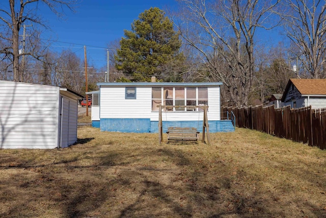 rear view of property with a yard, an outdoor structure, and fence