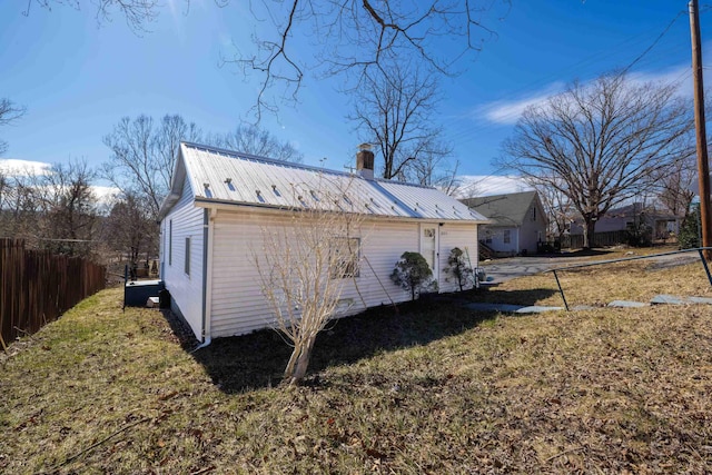 view of side of property featuring a yard, metal roof, a chimney, and fence