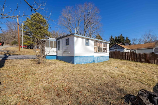 view of side of property featuring a sunroom, fence, and a lawn