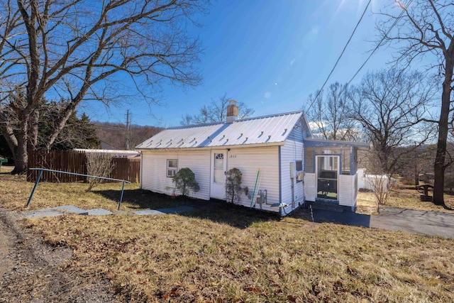 view of side of property featuring metal roof, a chimney, and fence