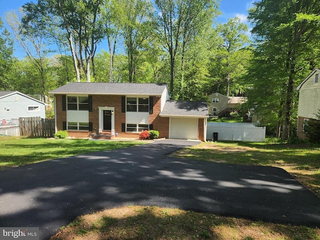 raised ranch featuring a front yard, fence, driveway, and brick siding