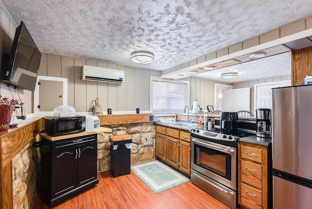 kitchen featuring sink, a wall mounted AC, stainless steel appliances, a textured ceiling, and light hardwood / wood-style flooring