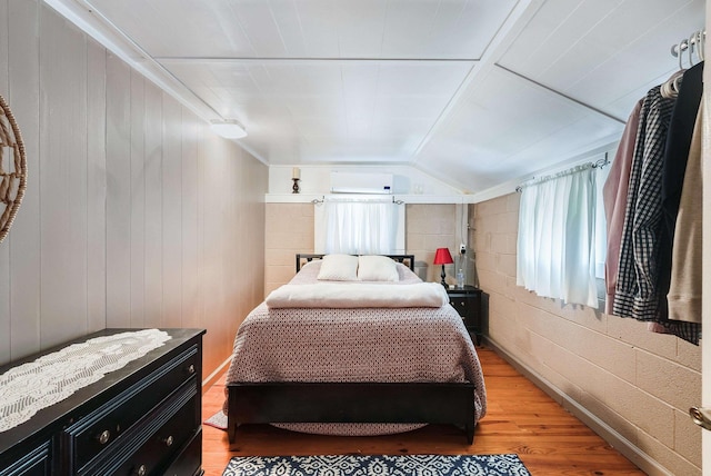 bedroom with wood-type flooring, vaulted ceiling, and a wall unit AC