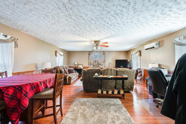 living room with ceiling fan, hardwood / wood-style flooring, a wall mounted AC, and a textured ceiling