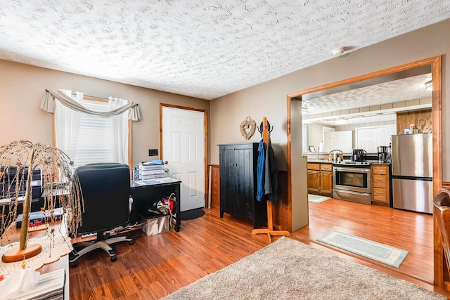 home office with light hardwood / wood-style flooring and a textured ceiling