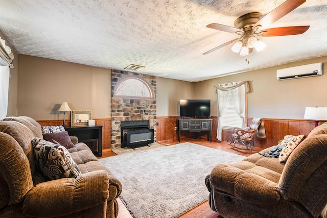 living room featuring ceiling fan, a wall mounted air conditioner, a fireplace, and a textured ceiling