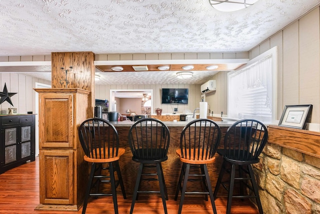 bar with a wall mounted AC, a textured ceiling, and dark hardwood / wood-style flooring